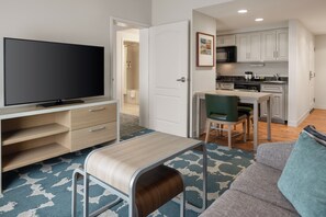 A modern living room with a flat-screen TV, a sofa, a coffee table, and a dining area with a chair and a small table.