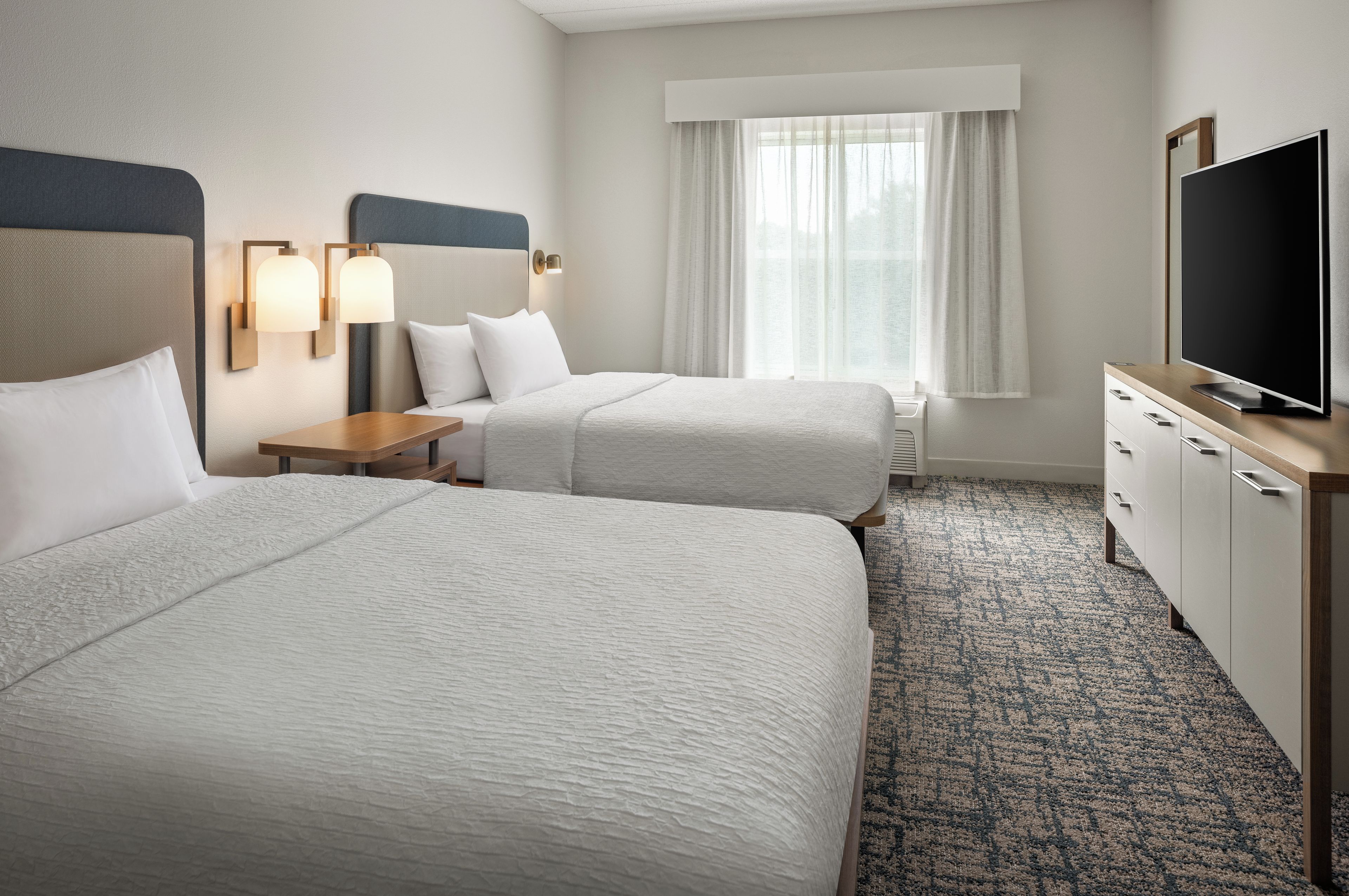 Quarto de hotel com duas camas, televisão, secretária e janela com cortinas.