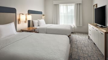 Quarto de hotel com duas camas, televisão, secretária e janela com cortinas.