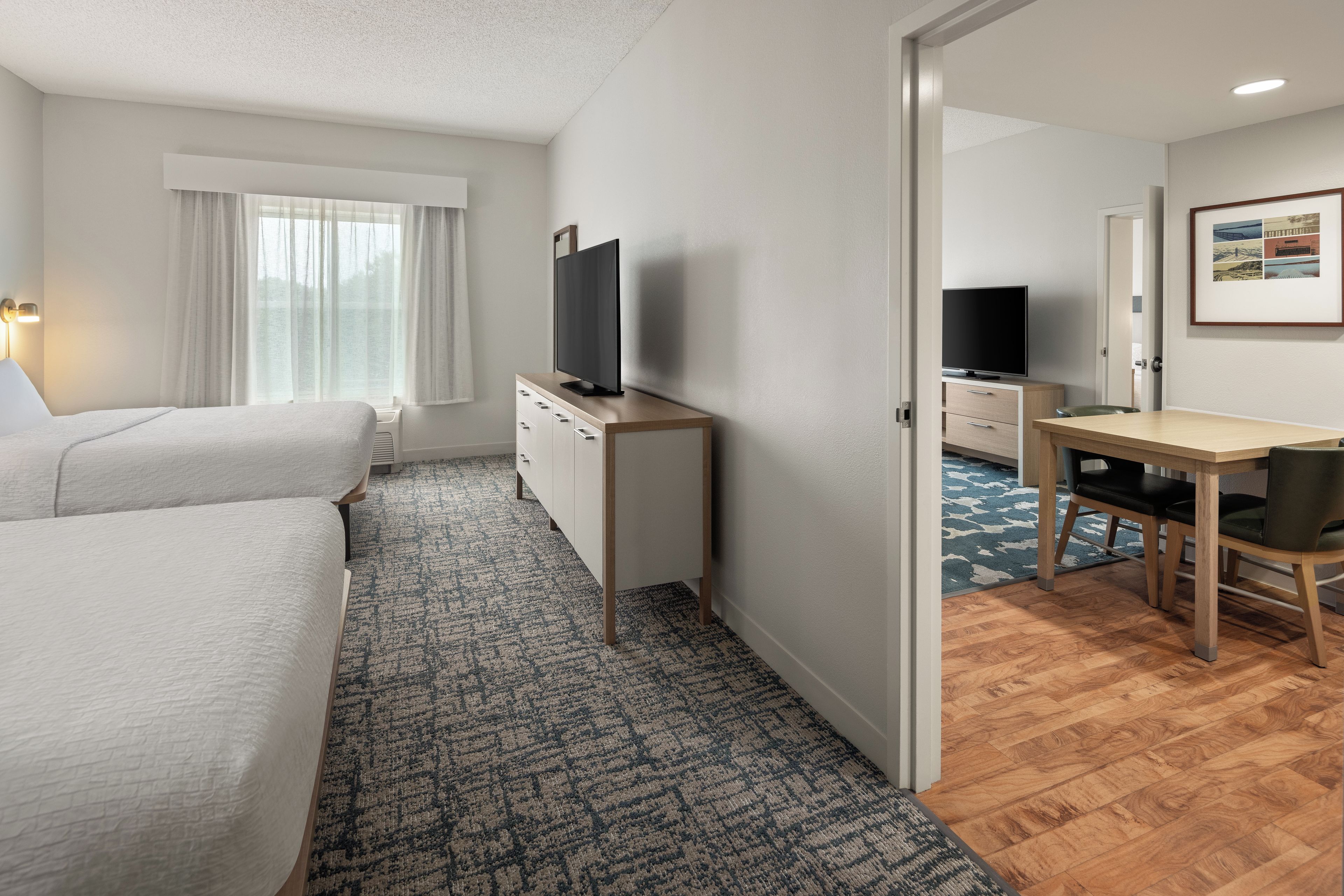 Una habitación de hotel con cama, escritorio, televisión y ventana con cortinas.