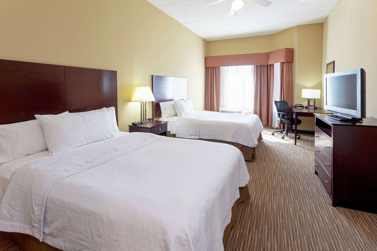 A hotel room with two beds, a desk with a television, and a chair.