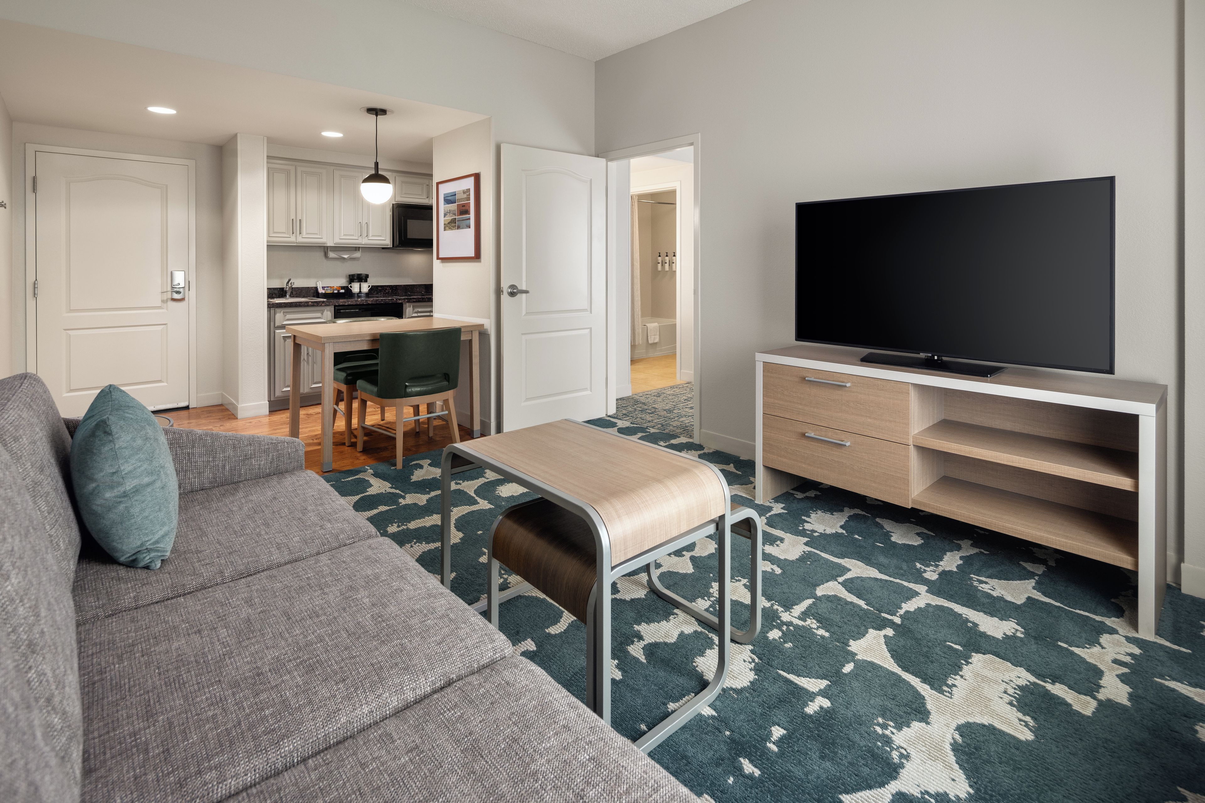 A modern living room with a grey sofa, a television on a stand, and a patterned carpet.