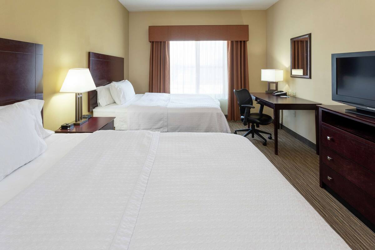 A hotel room with two beds, a desk, a chair, a television, and a window with curtains.