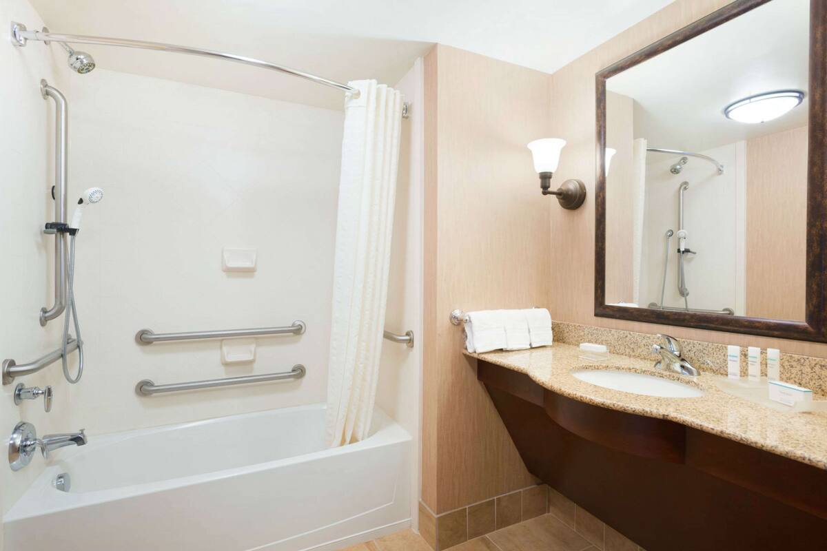A bathroom with a walk-in shower, grab bars, a sink with a mirror, and a towel rack.