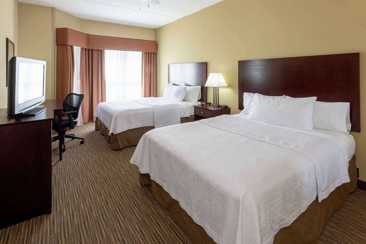 A hotel room with two beds, a desk with a television, a chair, and a lamp.