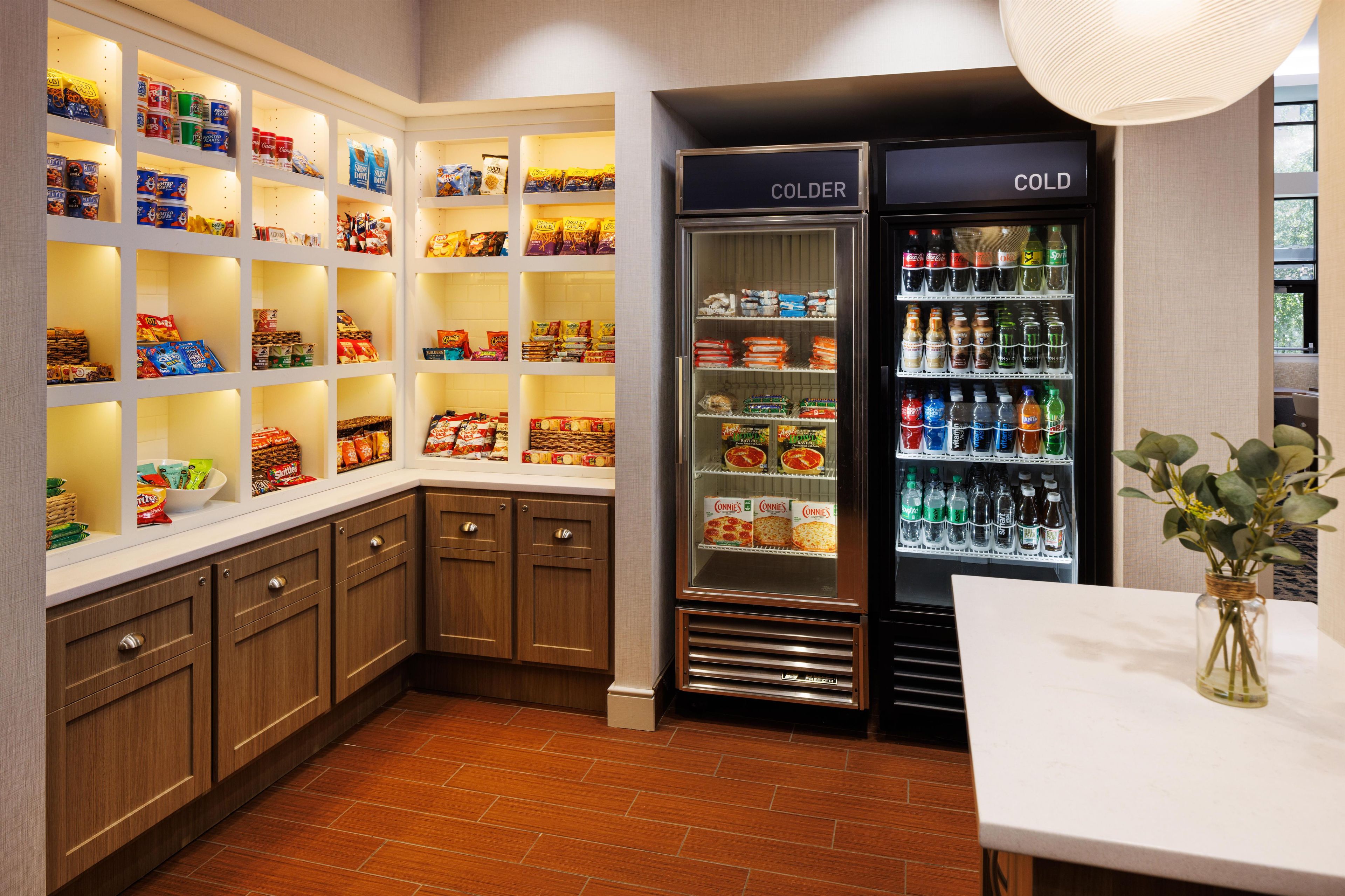 A kitchen with wooden cabinets, a built-in pantry with snacks, and a refrigerator with beverages.