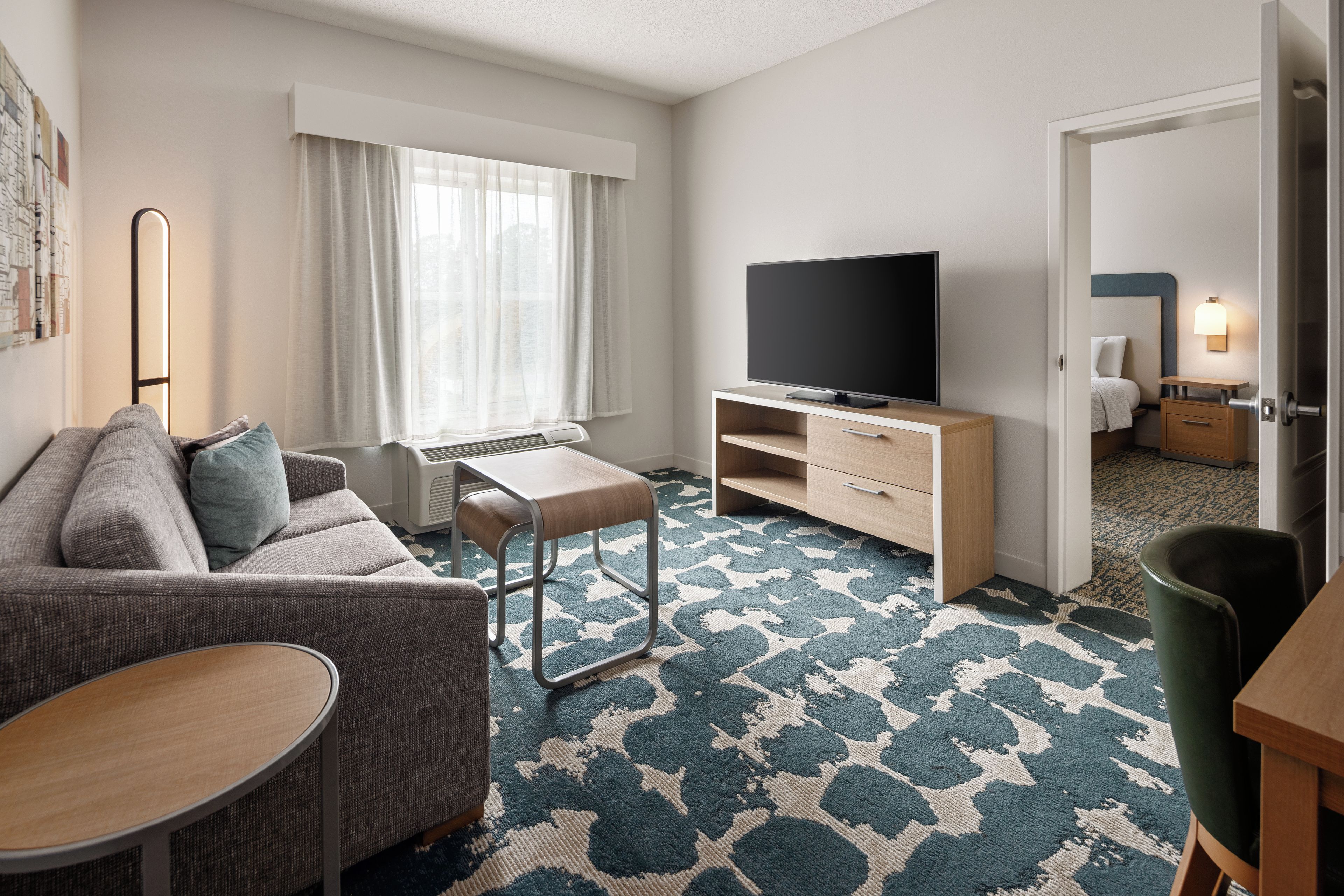 Habitación de hotel moderna con sofá, una mesita, televisor y alfombra estampada.