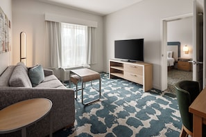 A modern hotel room with a sofa, a small table, a TV, and a patterned carpet. - Homewood Suites by Hilton St Louis Park at West End (St. Louis Park)