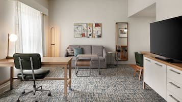 A modern living room with a sofa, a desk, a chair, a television, and artwork on the wall.