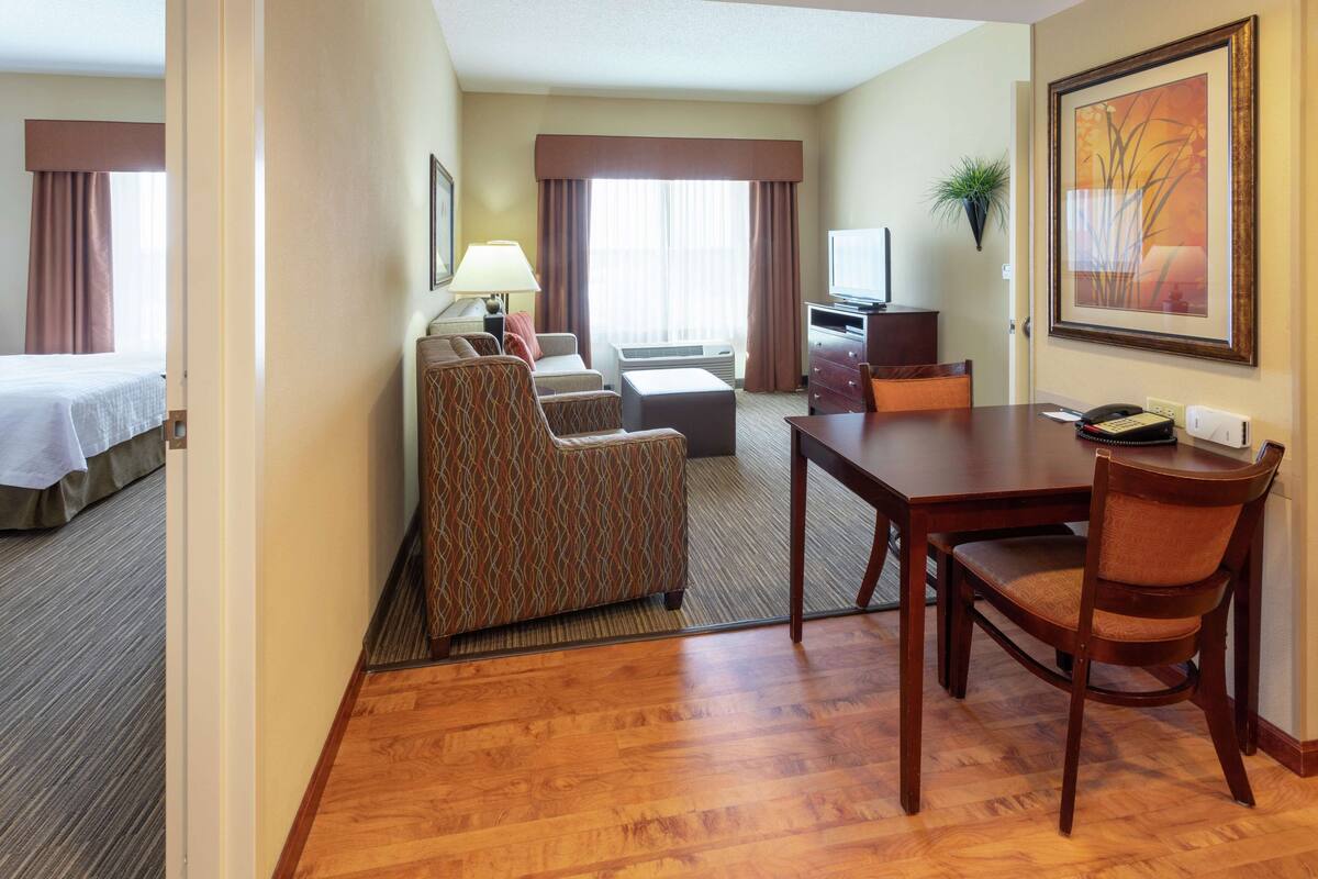 A hotel room with a bed, a sofa, a desk with a chair, a television, and a framed picture on the wall.