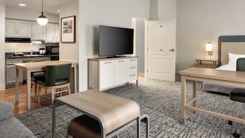 A compact hotel room with a kitchenette, a dining area, a TV, a bed, and a small seating area.
