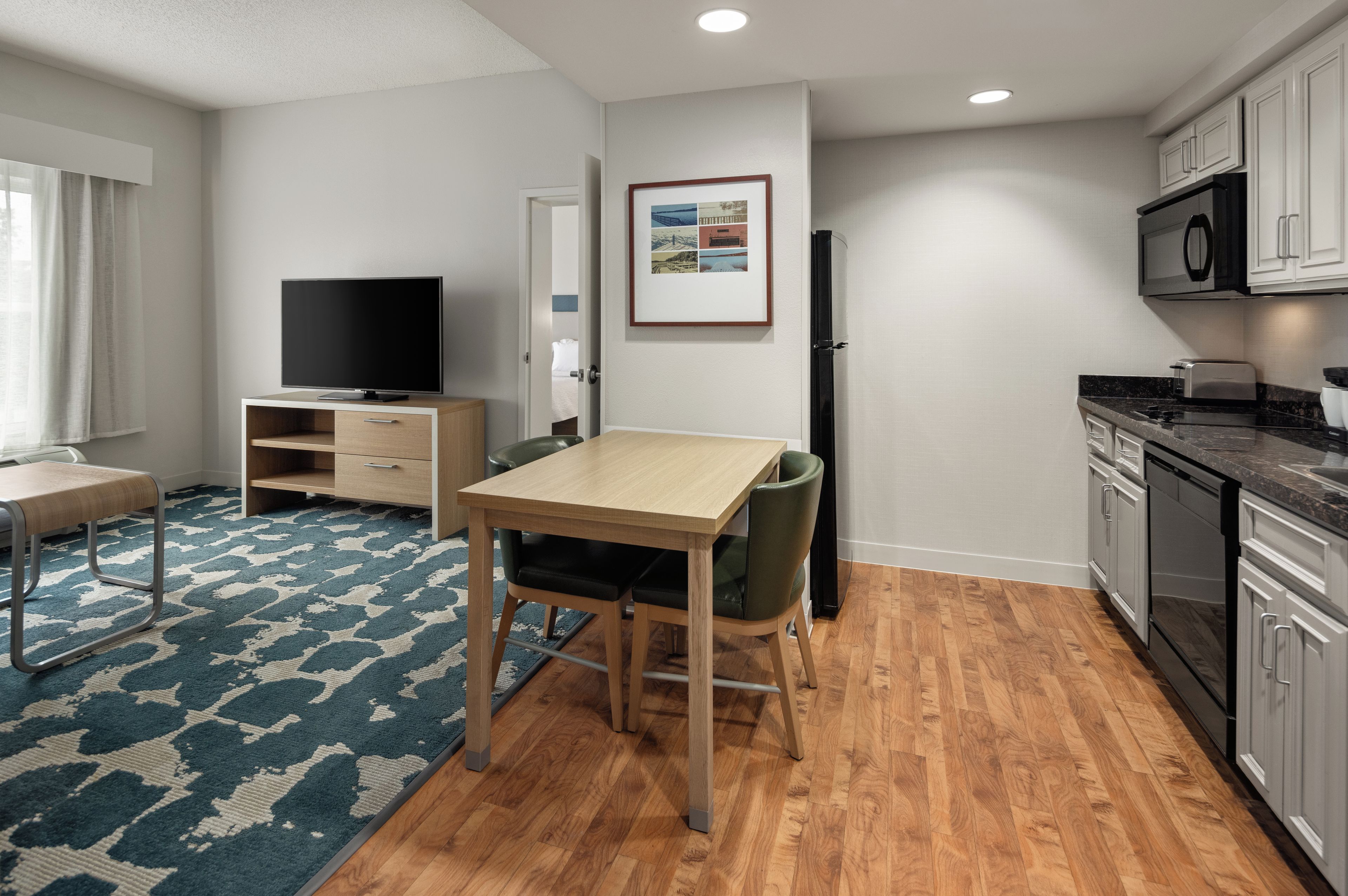 A modern kitchen with wooden cabinets, a built-in microwave, and a dining area with a table and chairs.