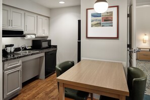 A compact kitchen with white cabinets, a black microwave, and a wooden dining table with two chairs.
