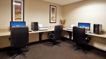 A hotel room with three desks, each with a computer and a printer, and a chair in the center.