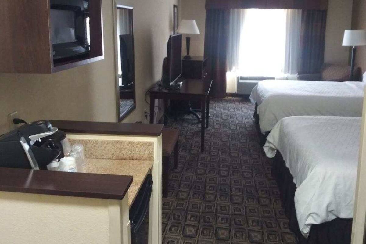 Ett hotellrum med två sängar, ett skrivbord med en dator, en tv och ett fönster med gardiner.