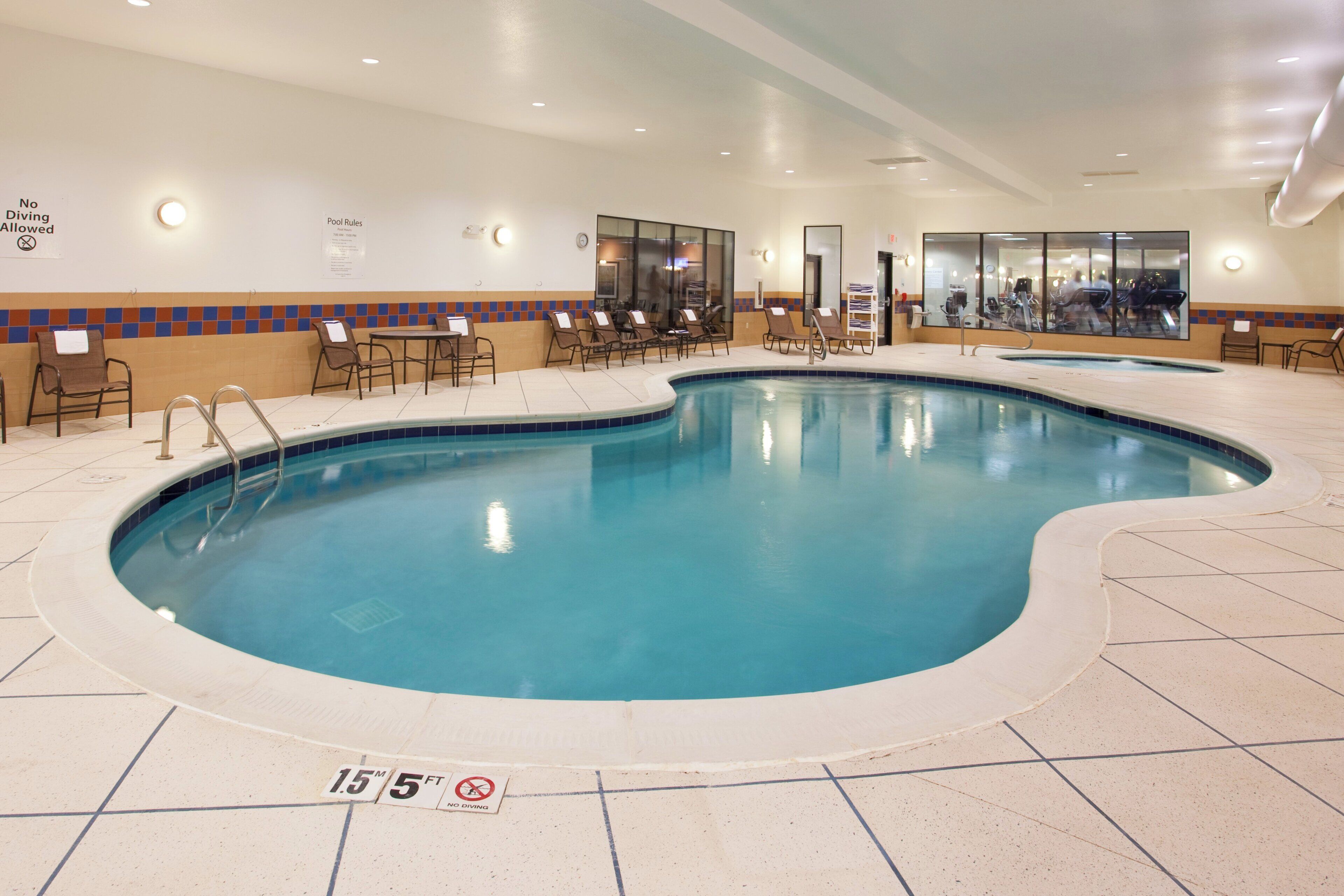 An indoor swimming pool with a tiled floor, lounge chairs, and a no diving sign.