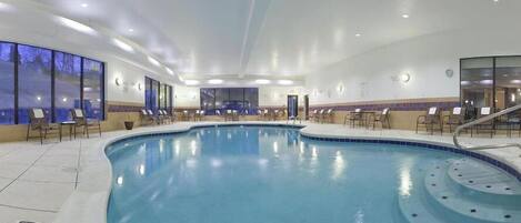 A large indoor swimming pool with multiple lounge chairs and a staircase leading to an upper level.