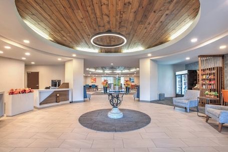 A spacious lobby with a central round table, seating area, and a reception desk.
