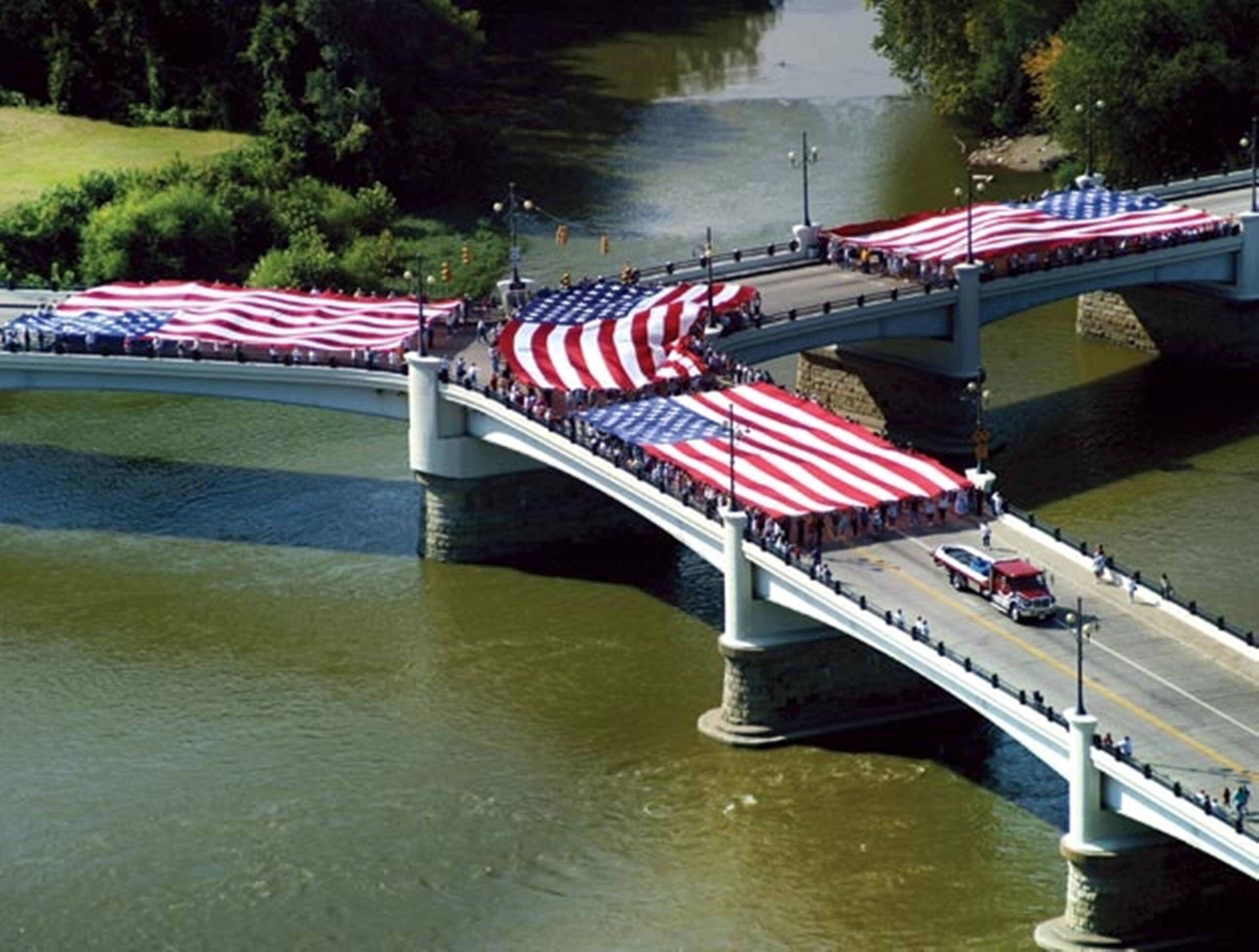 Un puente adornado con grandes banderas estadounidenses, con agua debajo y una carretera con vehículos.
