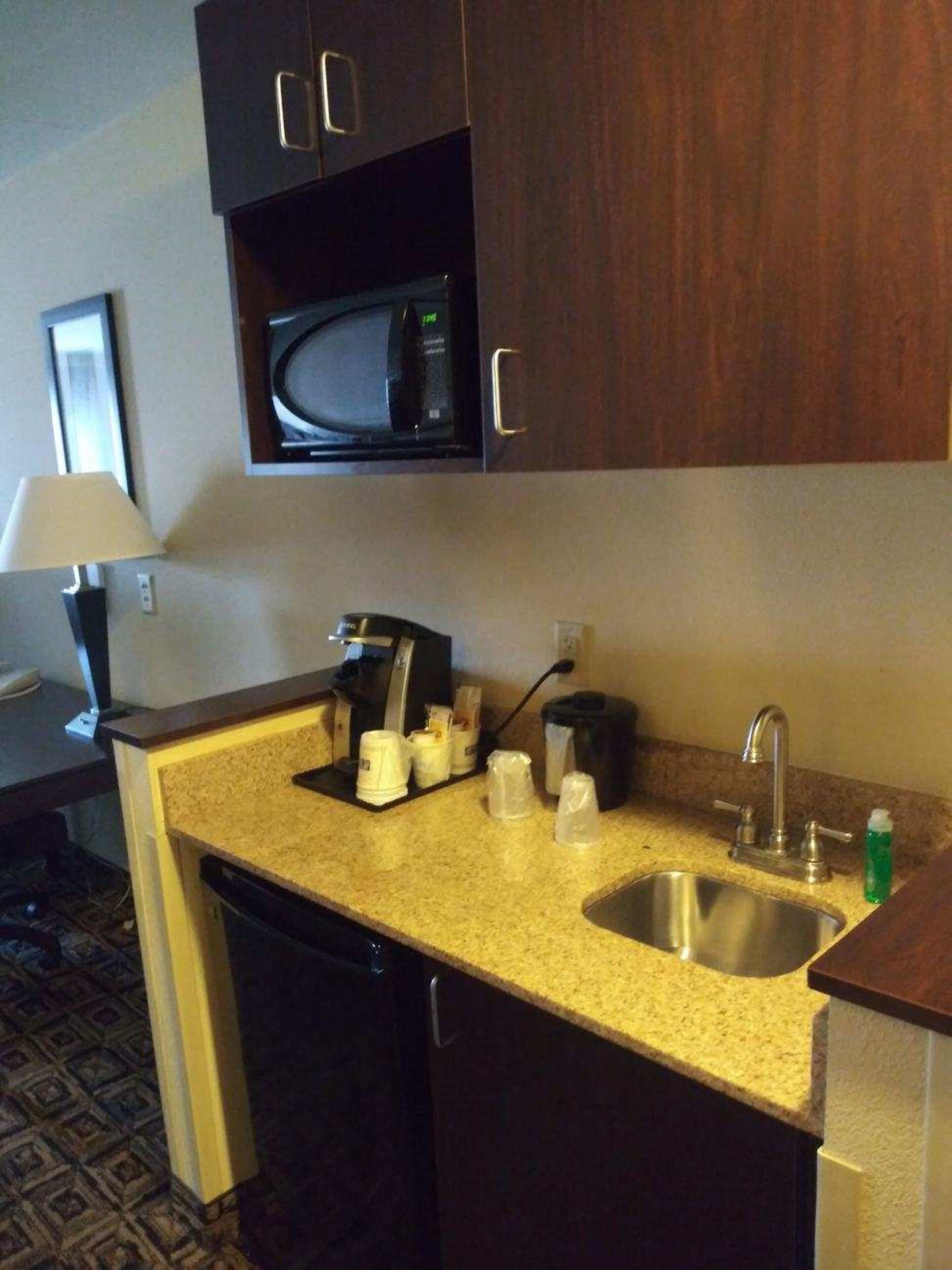 A compact kitchenette with a microwave, coffee maker, and a sink.