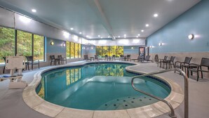 Una piscina interior de diseño curvo, rodeada de sillas y una zona de estar con vistas a árboles a través de amplios ventanales.