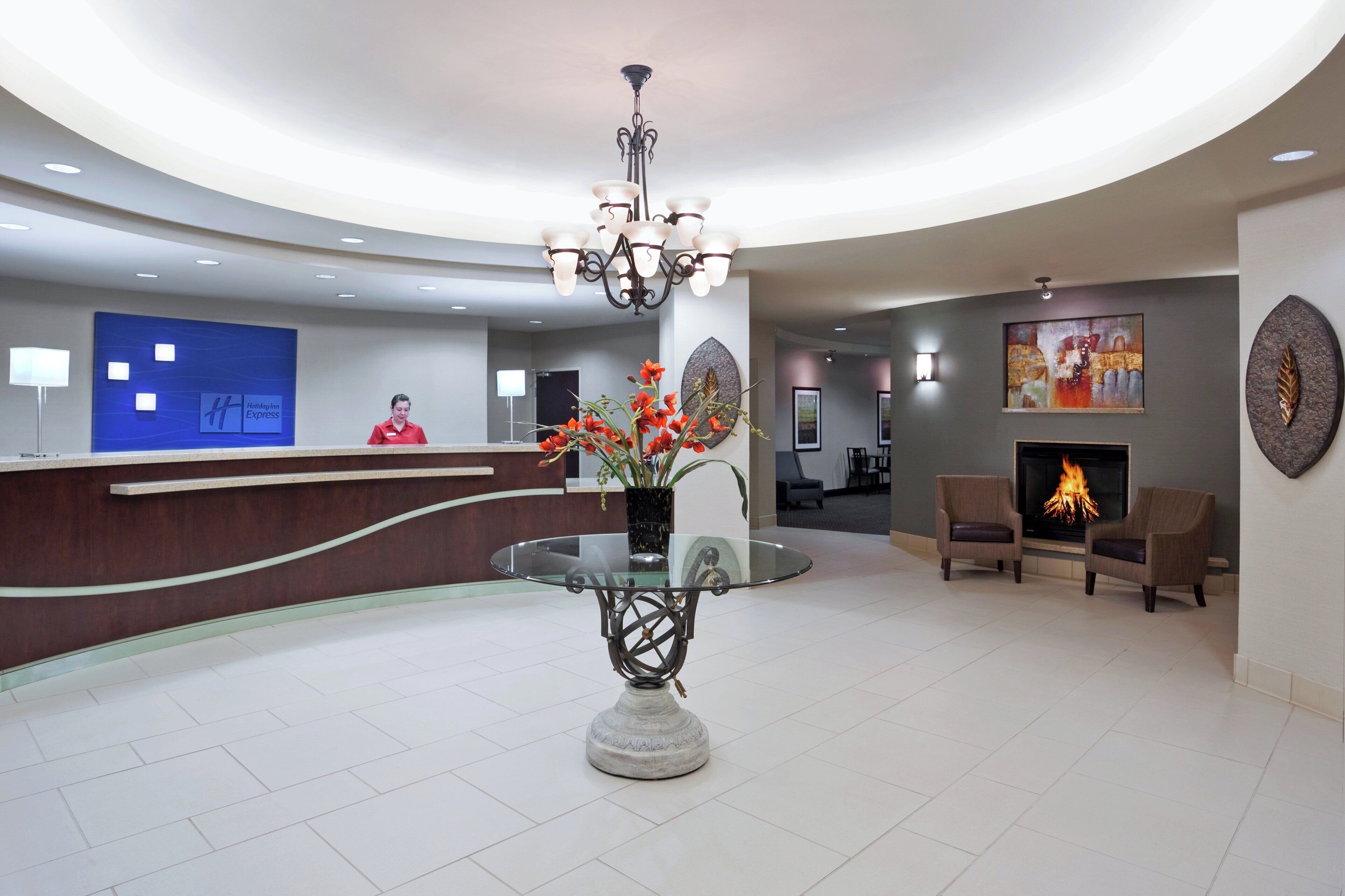 A hotel lobby with a reception desk, a glass-top table with a decorative centerpiece, a fireplace, and seating area.