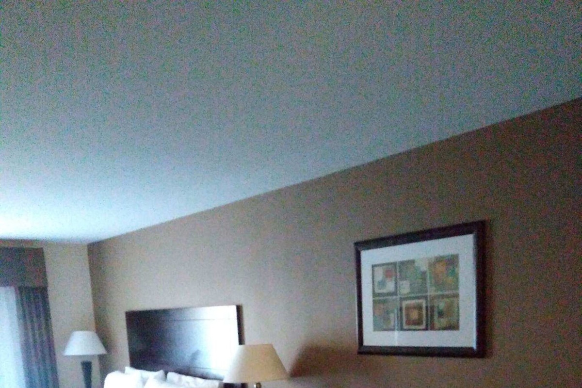 A hotel room with a bed, a sofa, a coffee table, a nightstand, and a framed picture on the wall.