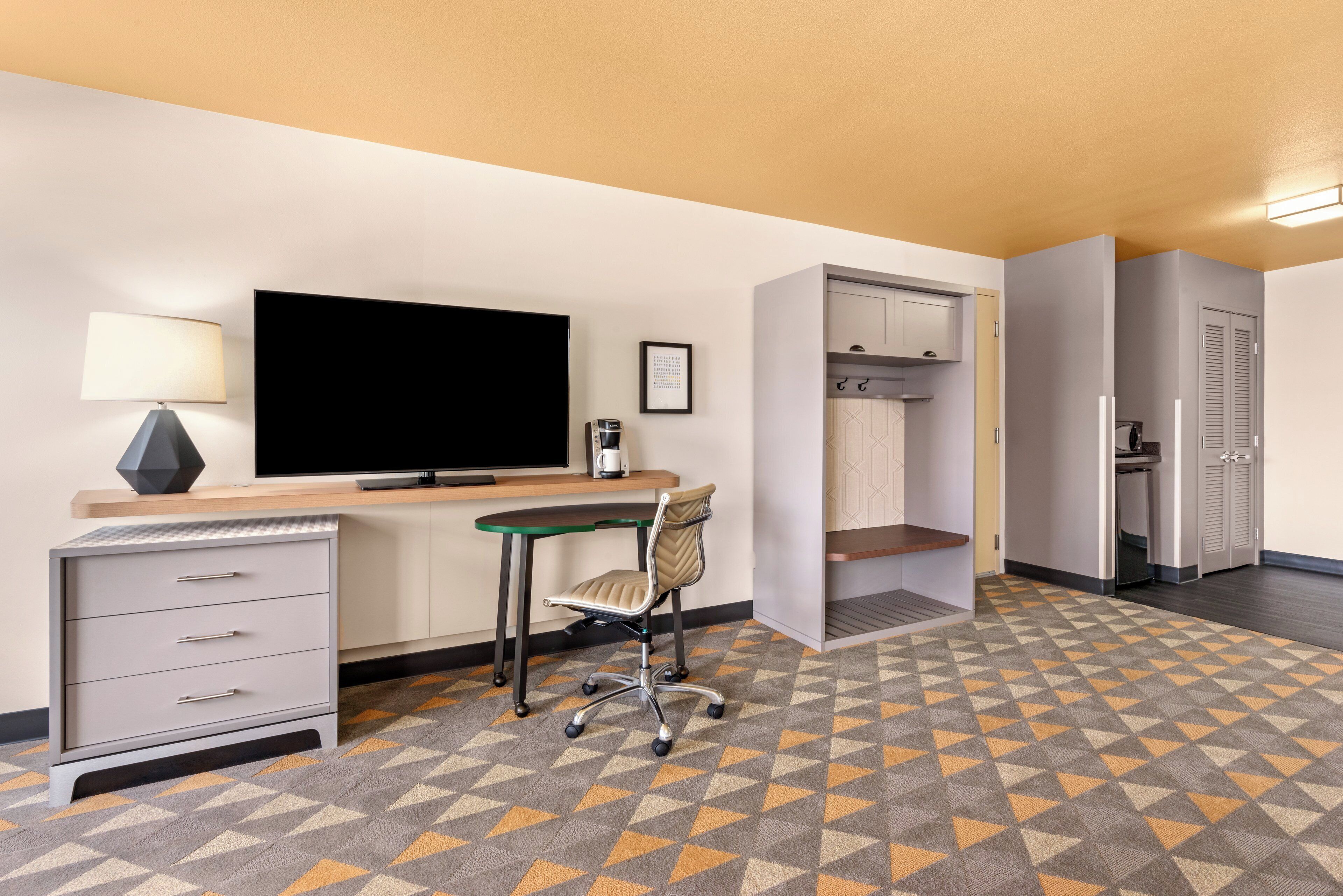 A hotel room with a desk, chair, television, minibar, and wardrobe.