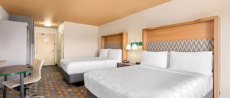 A hotel room with two beds, a desk, a chair, and a patterned carpet.