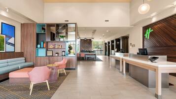 A modern hotel lobby with a reception desk, seating area, and a dining space.