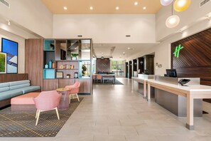 A modern hotel lobby with a reception desk, seating area, and a dining space.