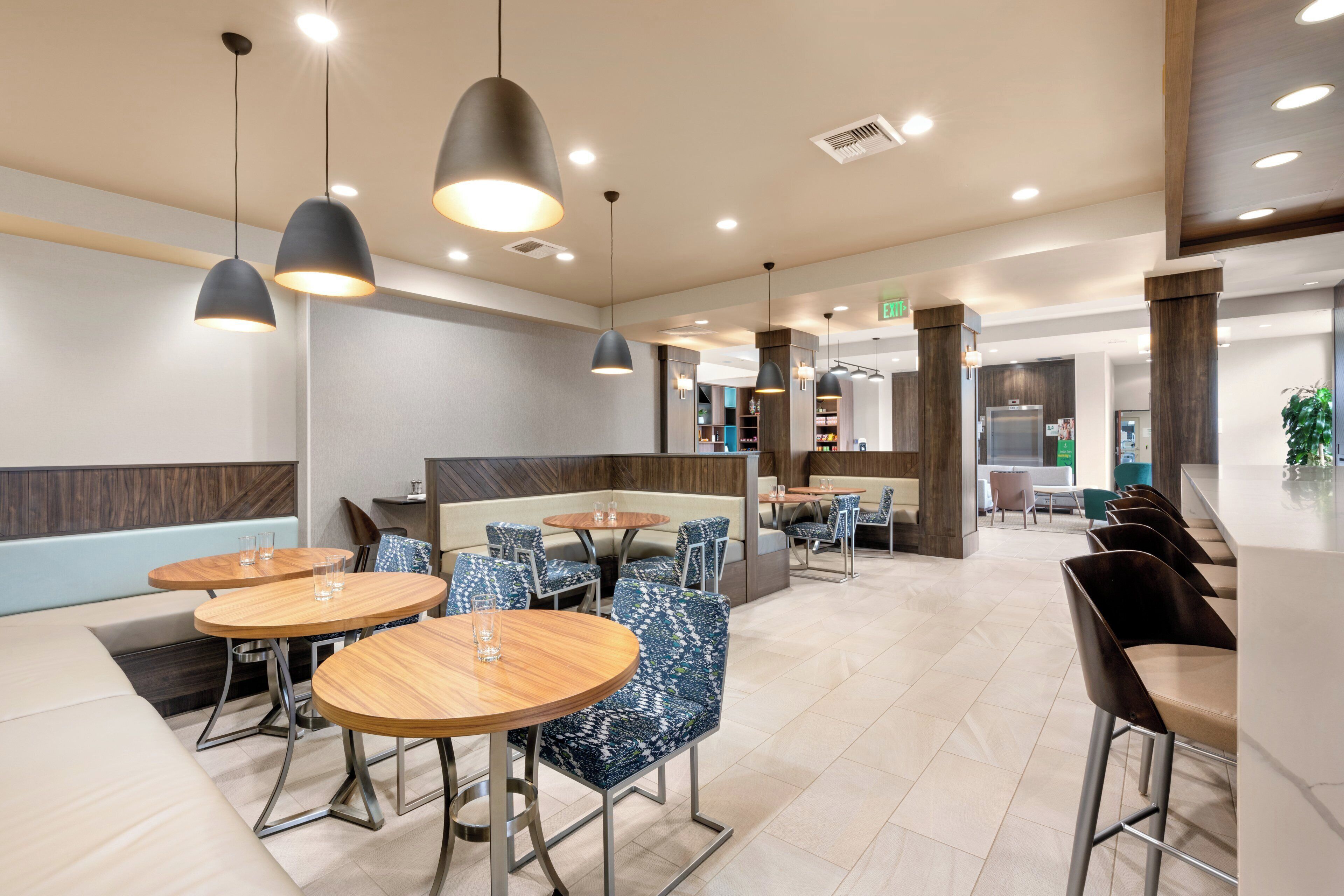 A modern restaurant interior with round tables, blue patterned chairs, and pendant lighting.