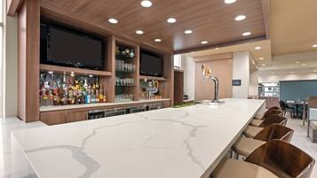 A modern bar area with a long counter, multiple seating options, and a television screen.