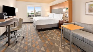 A hotel room with a bed, a desk with a computer, a sofa, and a large window with a city view. - Holiday Inn Yakima by IHG (Yakima)
