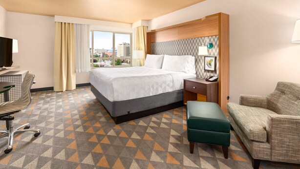 A hotel room with a large bed, a desk with a chair, a sofa, and a view of the city through the window. - Holiday Inn Yakima by IHG (Yakima)
