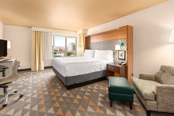 A hotel room with a large bed, a desk with a chair, a sofa, and a view of the city through the window. - Holiday Inn Yakima by IHG (Yakima)