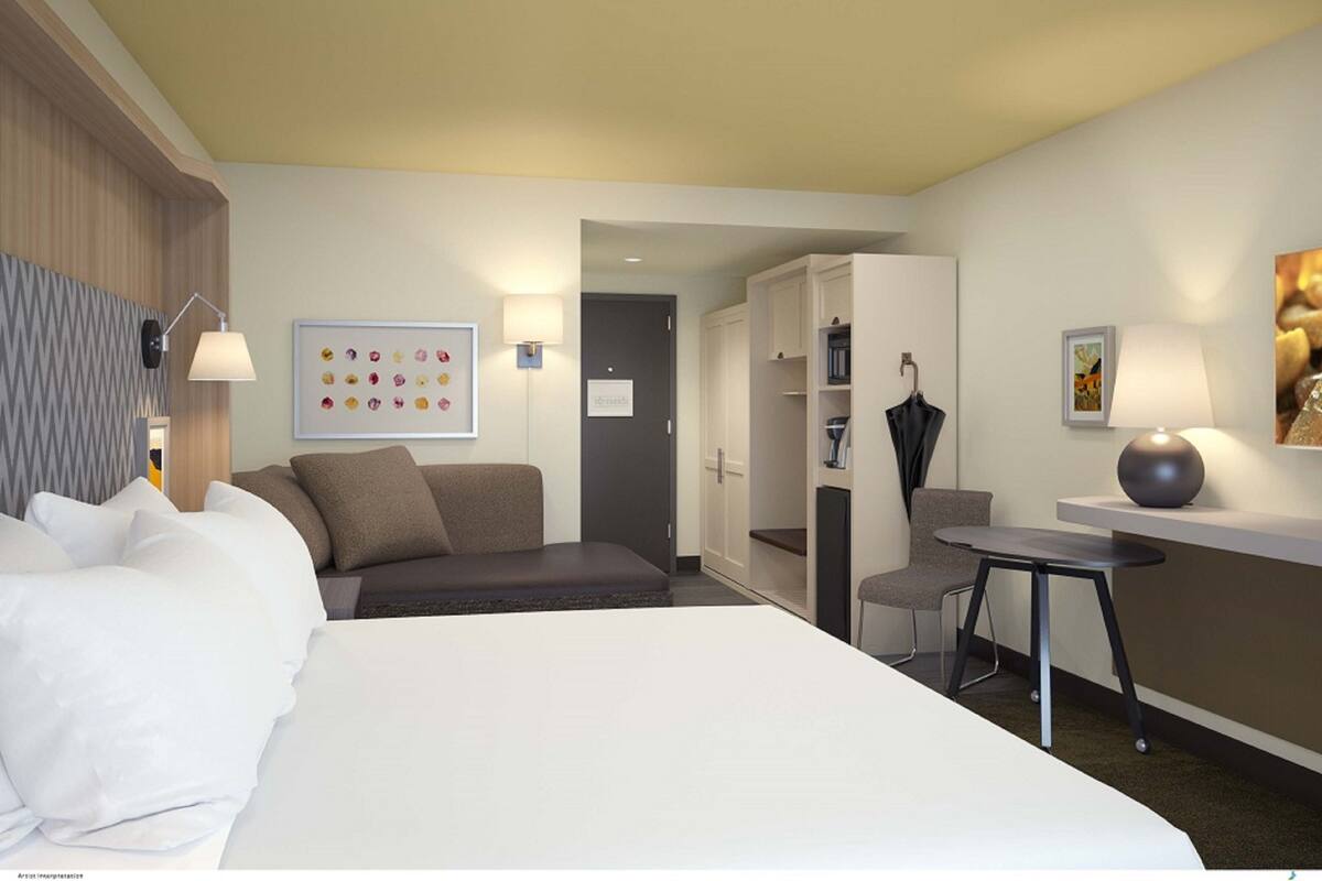 A modern hotel room with a large bed, a desk, a chair, and a wardrobe.