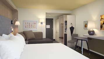 A modern hotel room with a large bed, a desk, a chair, and a wardrobe.