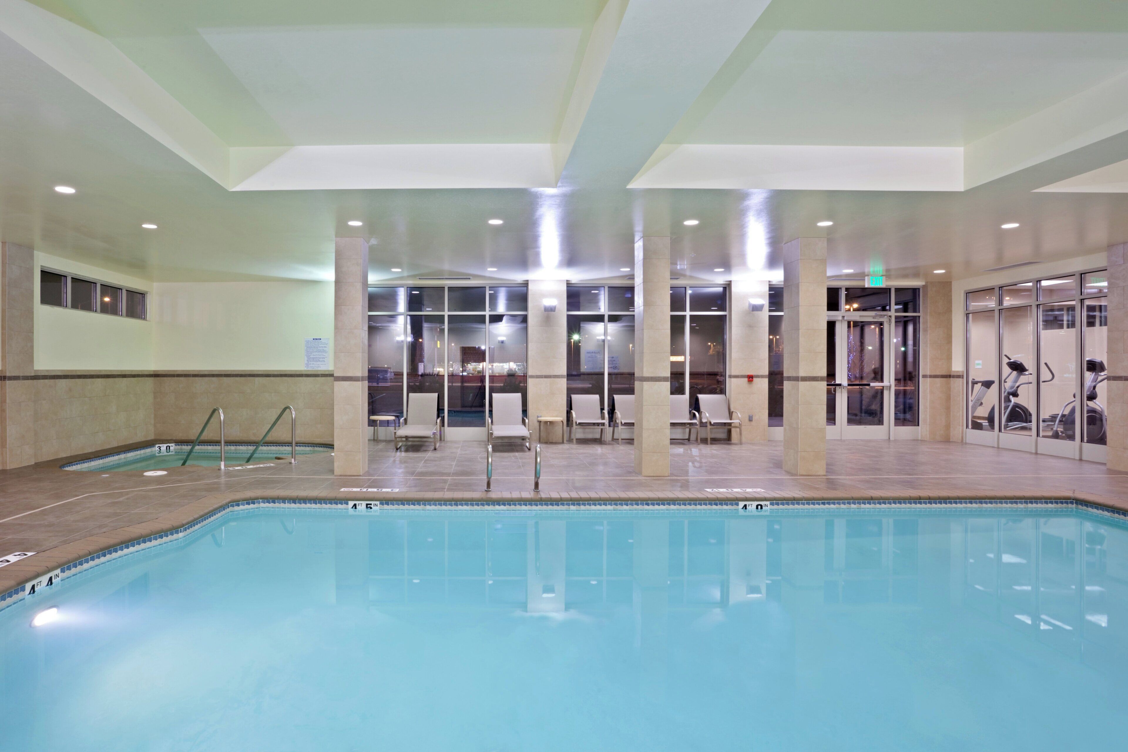 Una piscina interior con agua cristalina, rodeada de sillas de descanso y equipo de ejercicio.