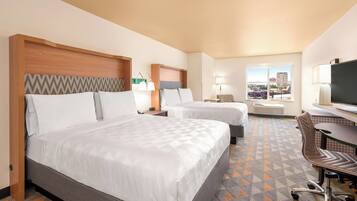 A hotel room with two beds, a desk, a chair, a TV, and a window with a city view.