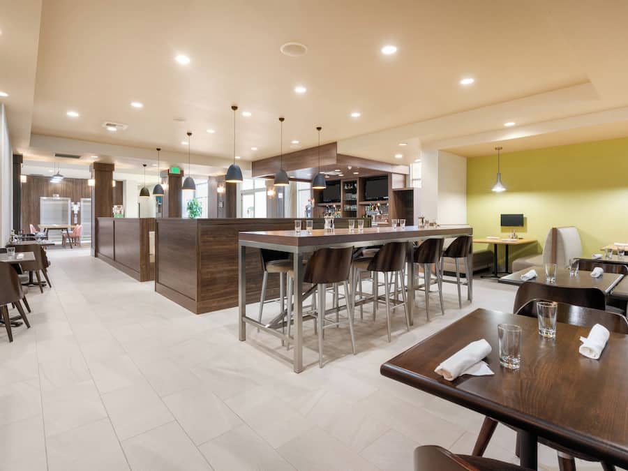 Een modern restaurant met een bar, hoge plafonds en veel licht.