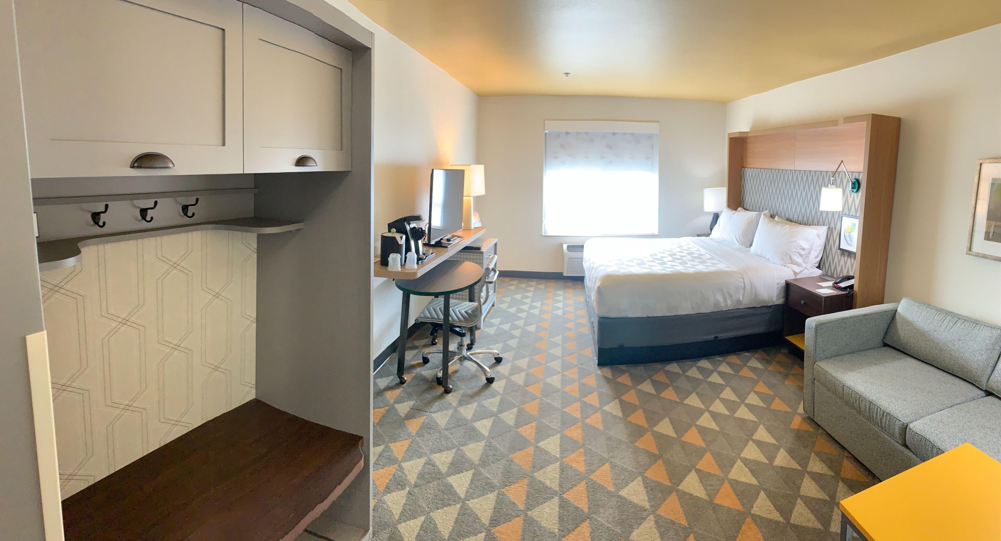 A hotel room with a bed, a desk with a computer, a sofa, and a small table.