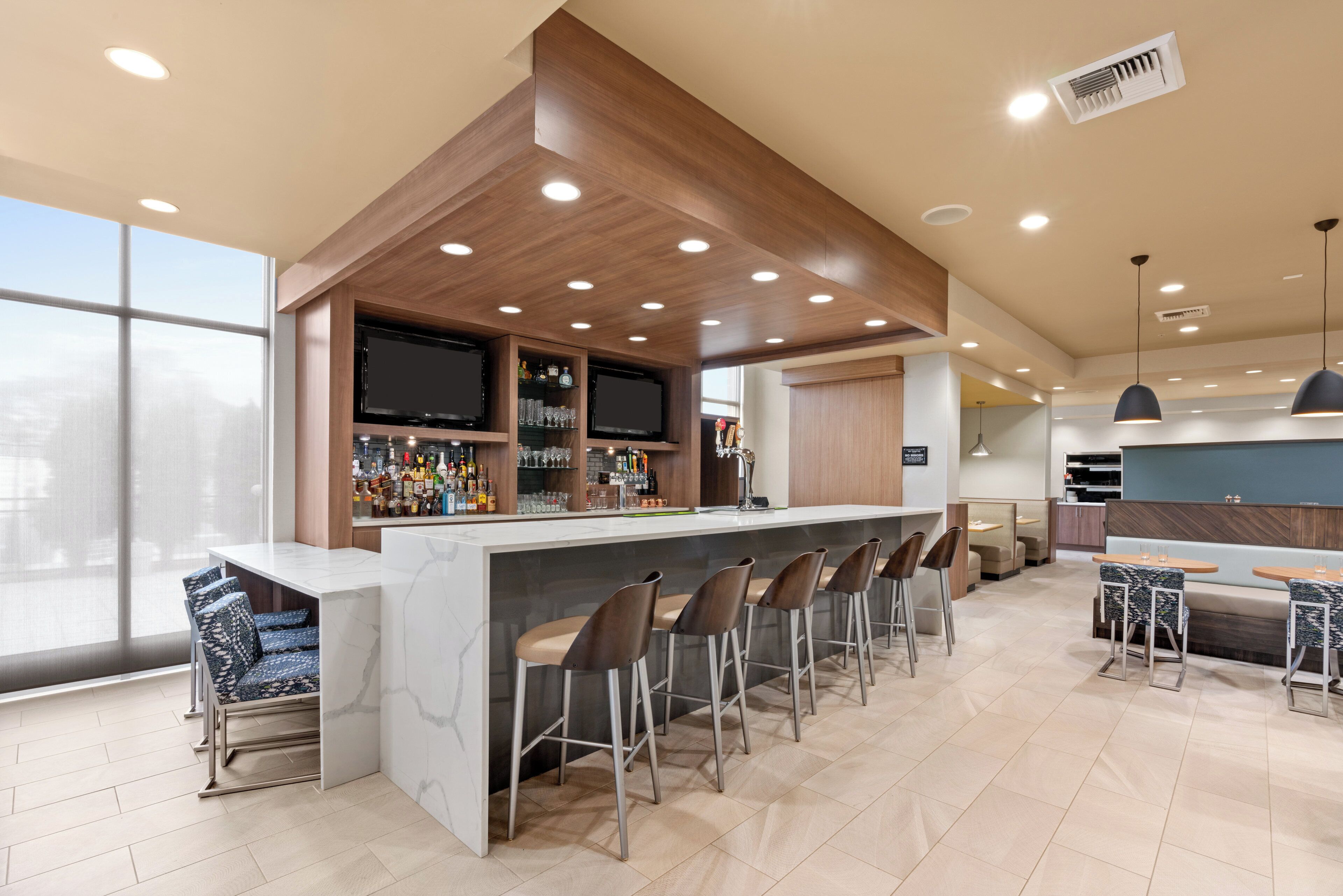 A modern bar area with a marble countertop, multiple stools, and a television mounted above the bar.