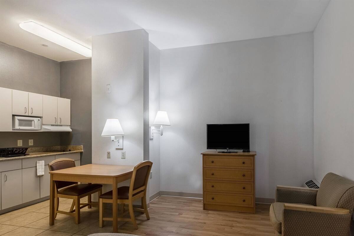 A compact living space with a kitchenette, a dining table with chairs, a TV on a wooden stand, and a sofa.