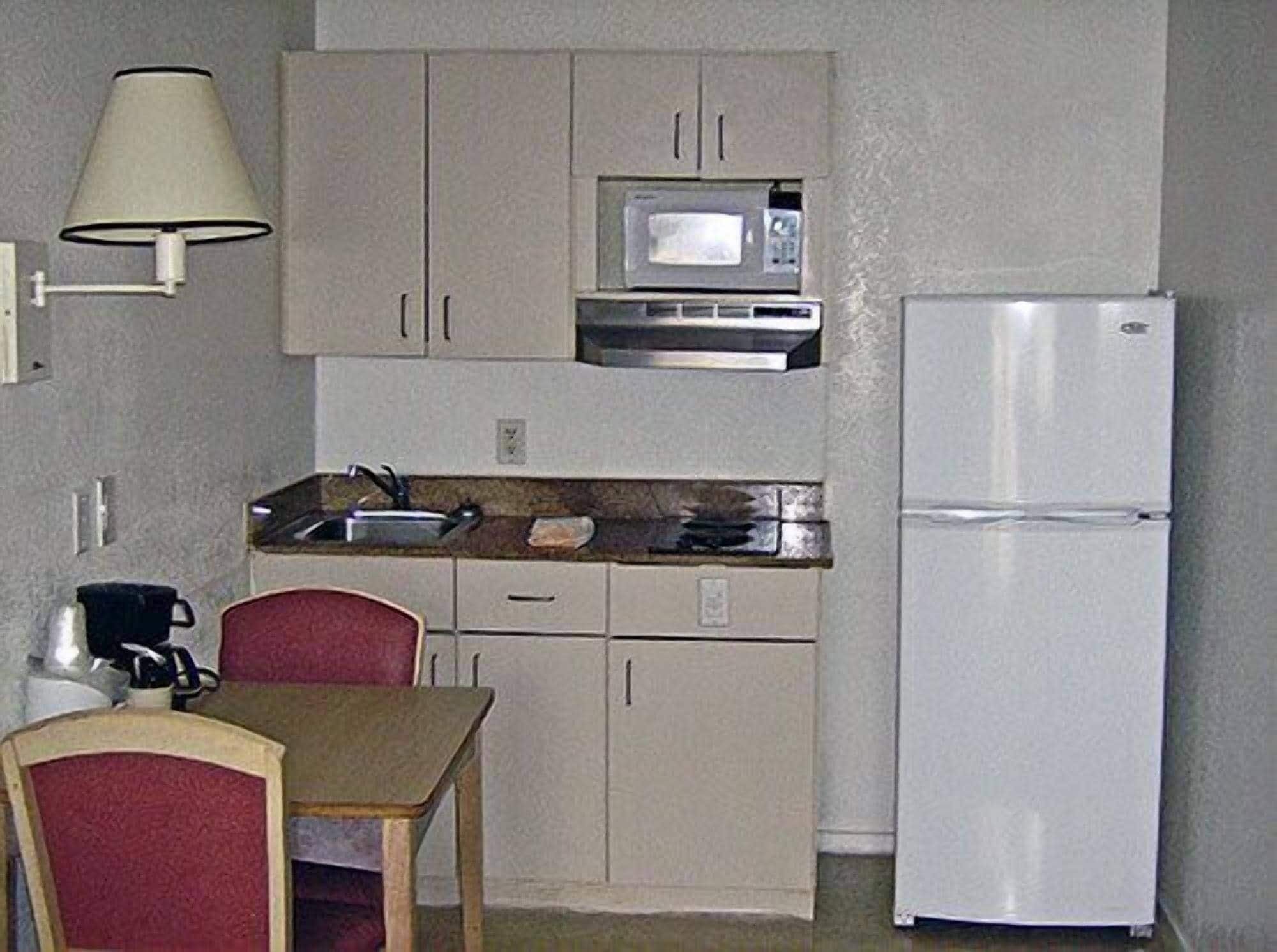 A compact kitchen with a microwave, refrigerator, sink, and a dining area with a table and chairs.