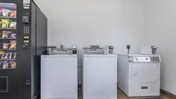 Une laverie équipée de trois machines à laver blanches et d’un distributeur automatique de collations.