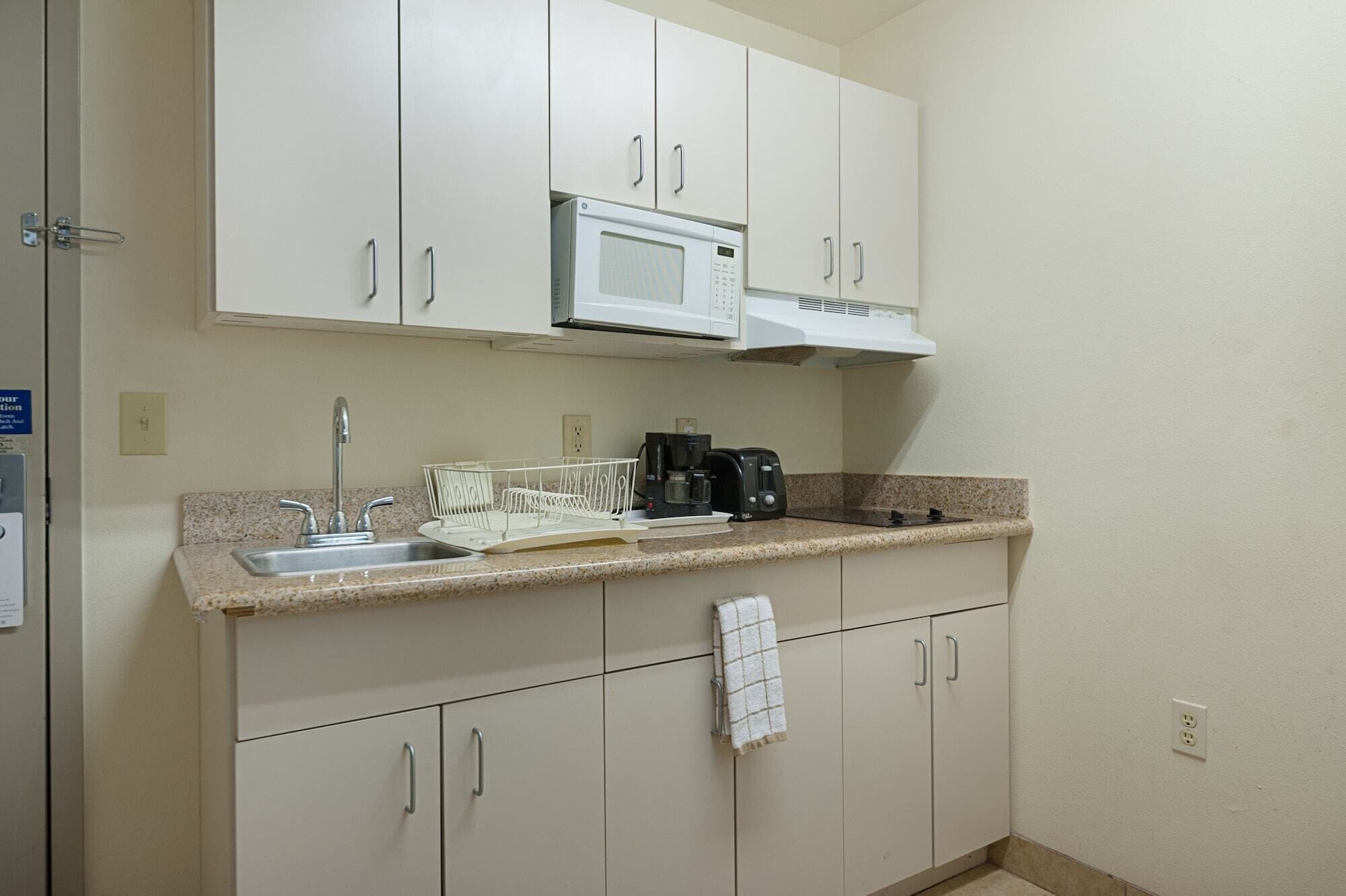 A compact kitchen with white cabinets, a microwave, a coffee maker, and a sink.