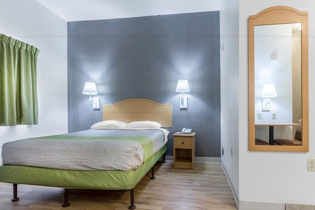 A neatly arranged hotel room with a bed, bedside lamps, a bedside phone, a small wooden nightstand, and a large mirror on the wall.