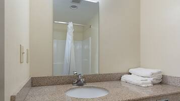 Un baño con lavamanos de granito, un espejo y una pila de toallas blancas.