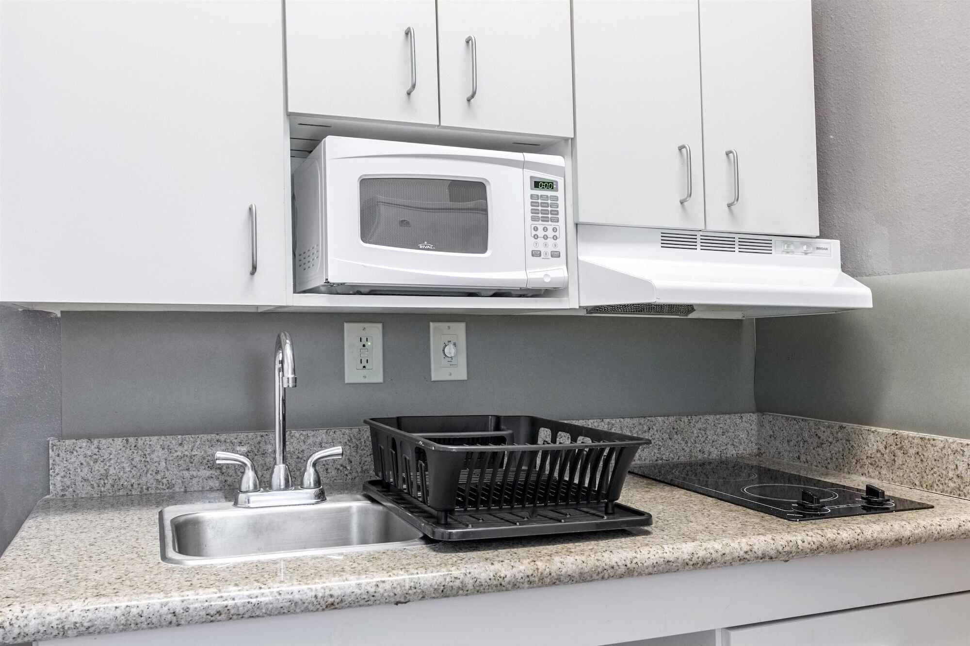 A kitchen with white cabinets, a microwave, a stove, and a sink with a granite countertop.